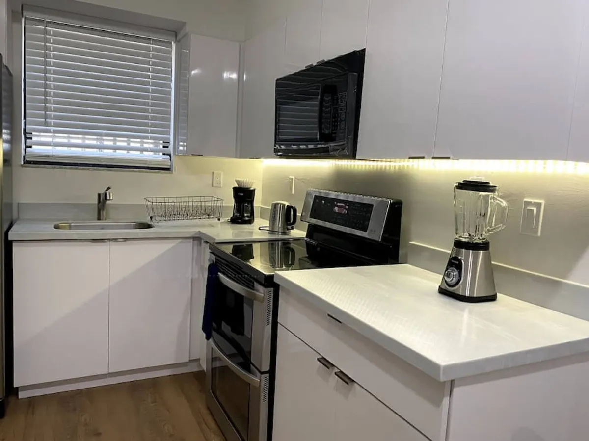 A modern kitchen setup featuring a stainless steel stove and oven, a black microwave mounted above, a blender on the countertop, and under-cabinet LED strip lighting. The space appears functional and inviting, making it ideal for meal preparation and casual gatherings.
